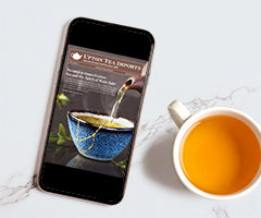 Smartphone displaying a tea company's website next to a cup of tea on a marble surface