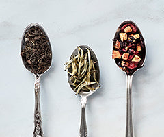 Three spoons with different types of tea leaves on a light background